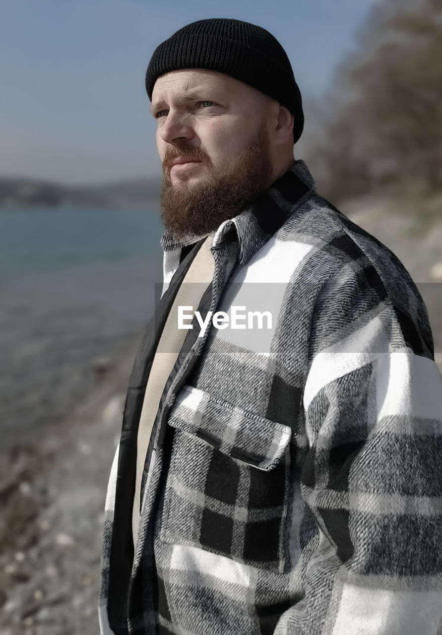 one person, adult, men, portrait, nature, beard, water, clothing, land, facial hair, standing, sea, young adult, waist up, beach, sky, looking, leisure activity, day, looking away, person, focus on foreground, hat, casual clothing, outdoors, lifestyles, contemplation, spring, relaxation, emotion, smiling, front view