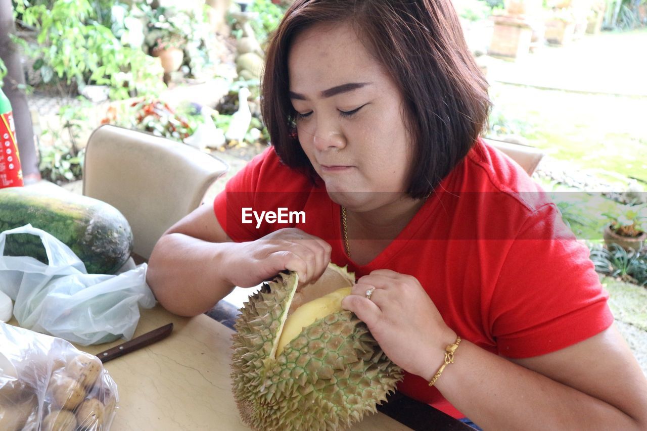 Woman opening durian on table sitting in yard