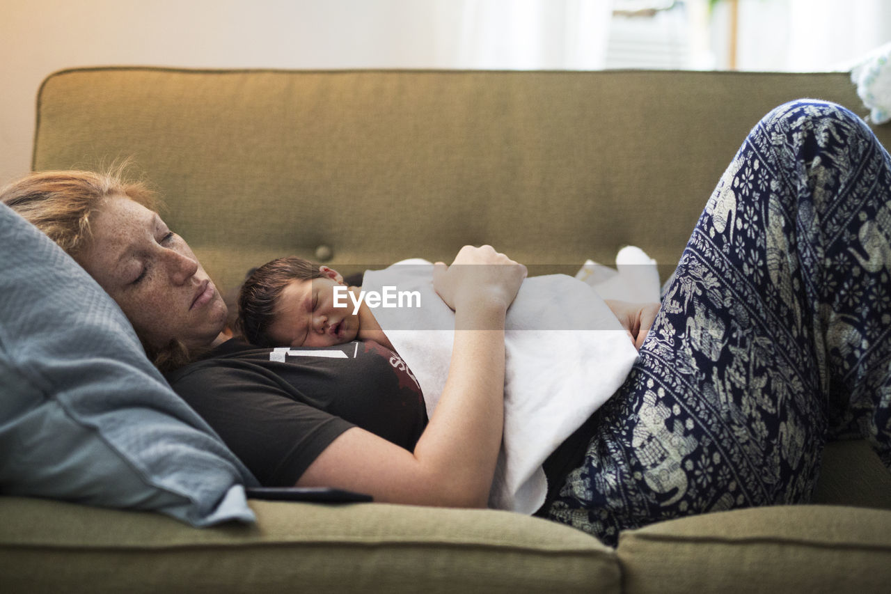 Side view of woman sleeping with baby boy on sofa at home