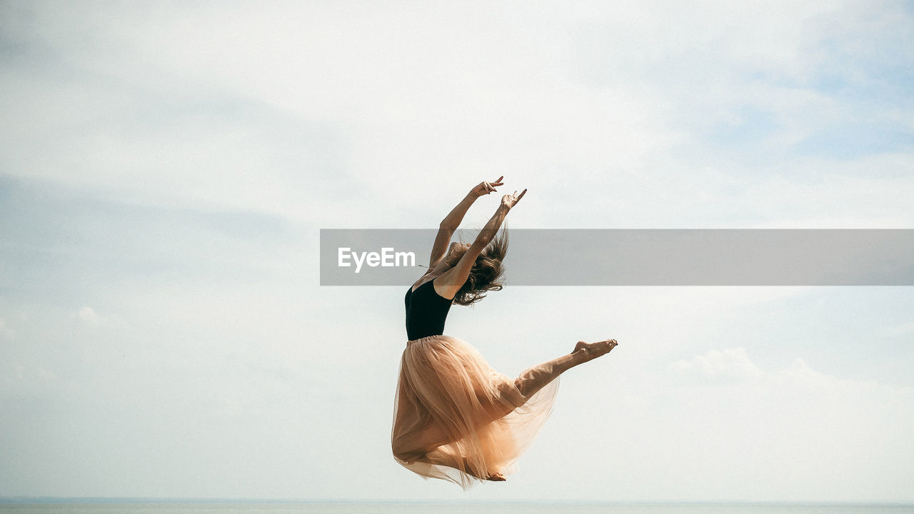 Woman dancing over sea against sky