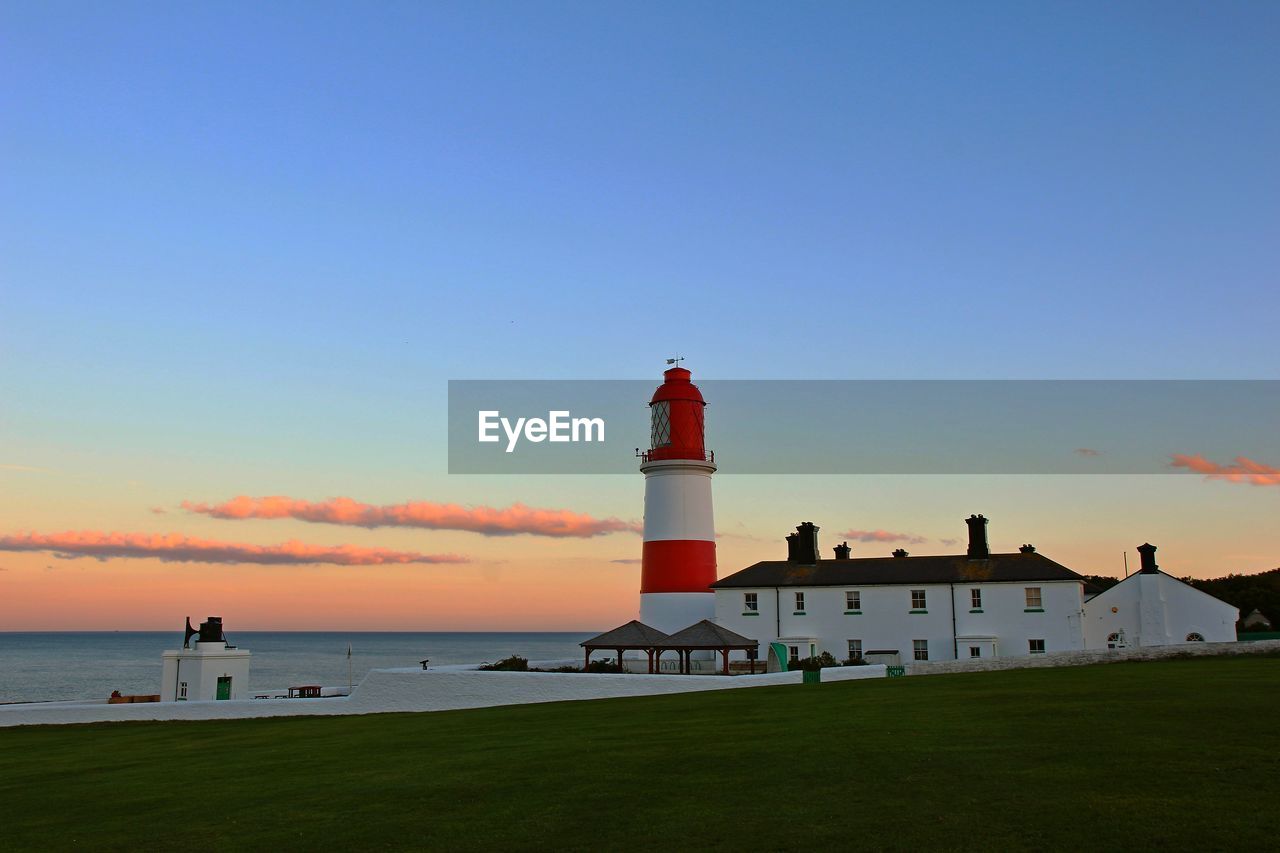 Lighthouse by sea and buildings against sky