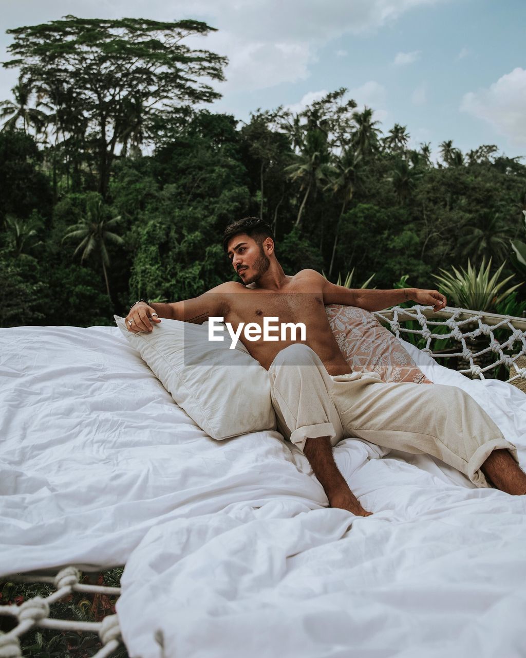 Shirtless young man relaxing on bed against trees in forest
