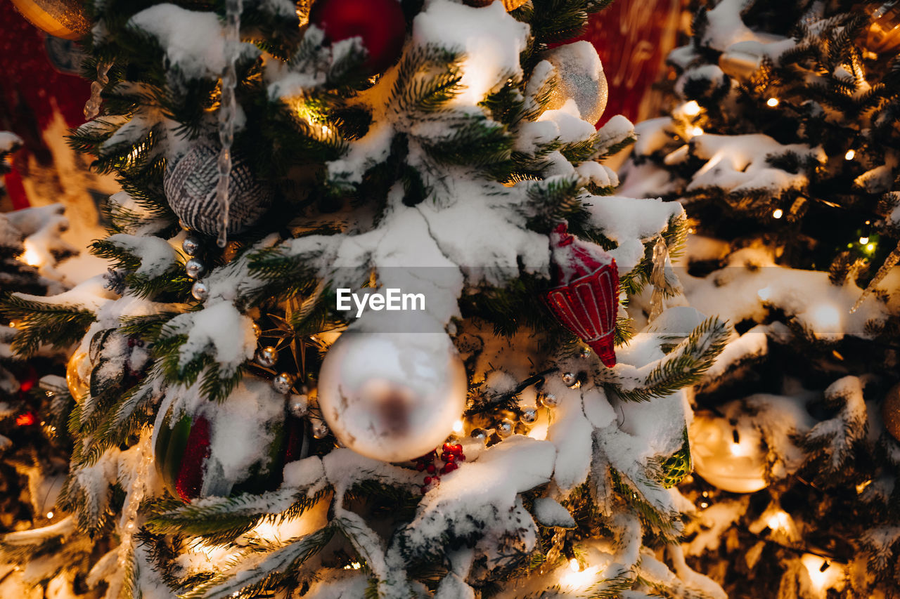 Snow covered christmas tree decorated with golden festive balls, toys and lights. new year 2022 