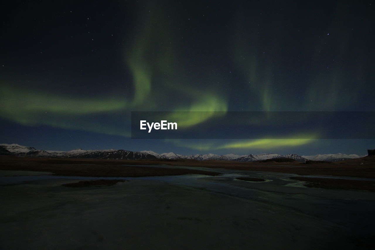 Low angle view of aurora borealis over mountains and lake