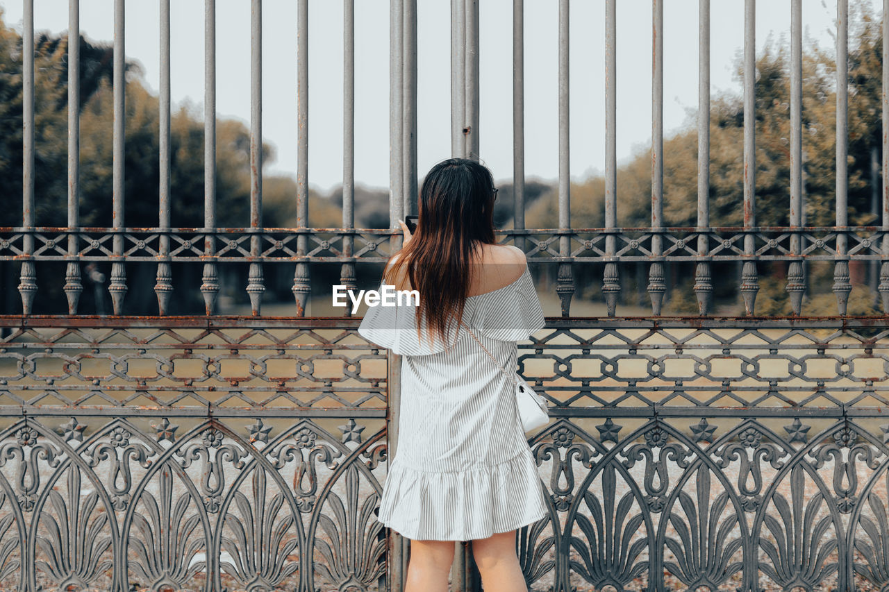 Rear view of woman standing by chainlink fence