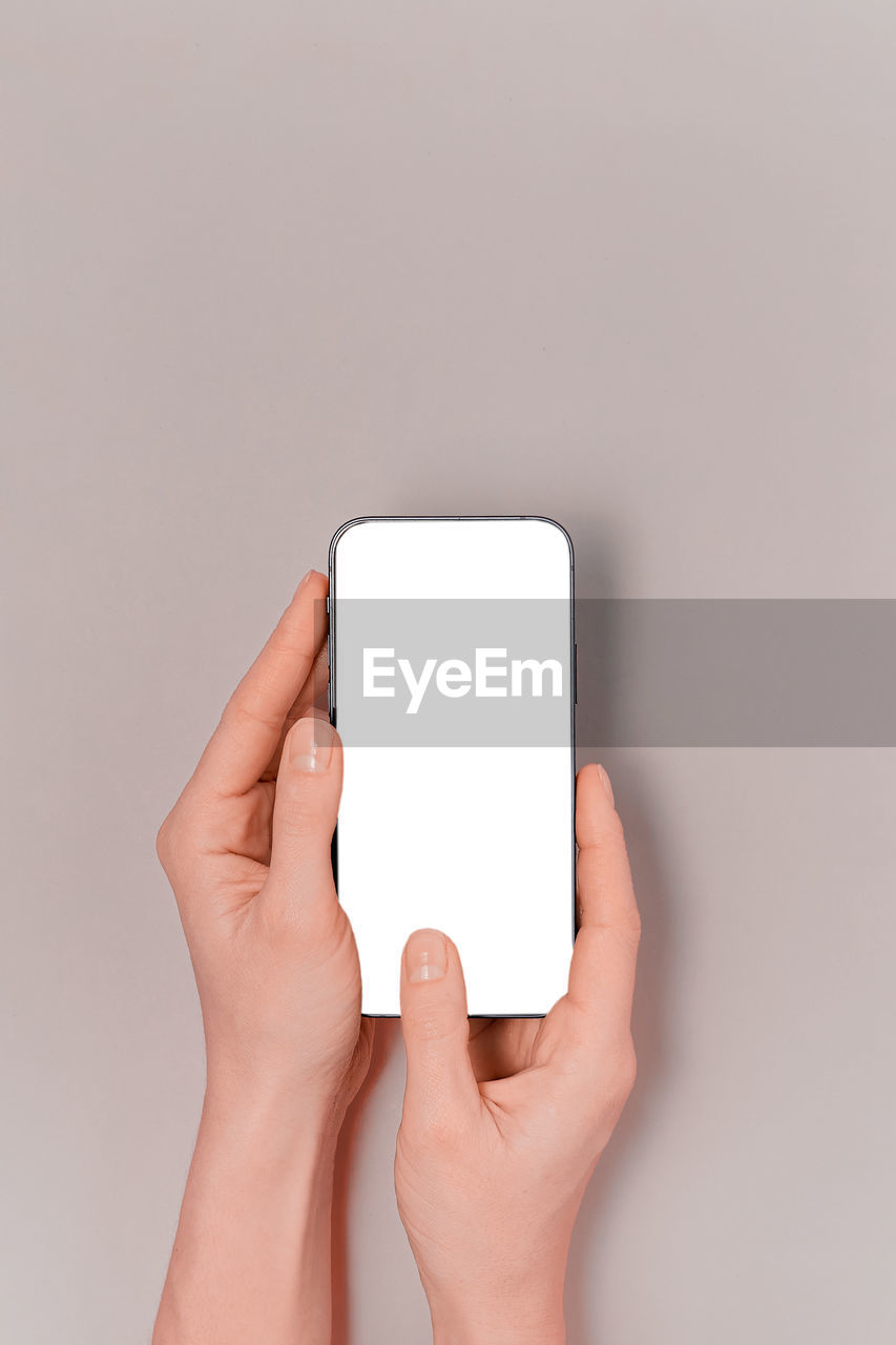 cropped hands of woman using mobile phone against gray background