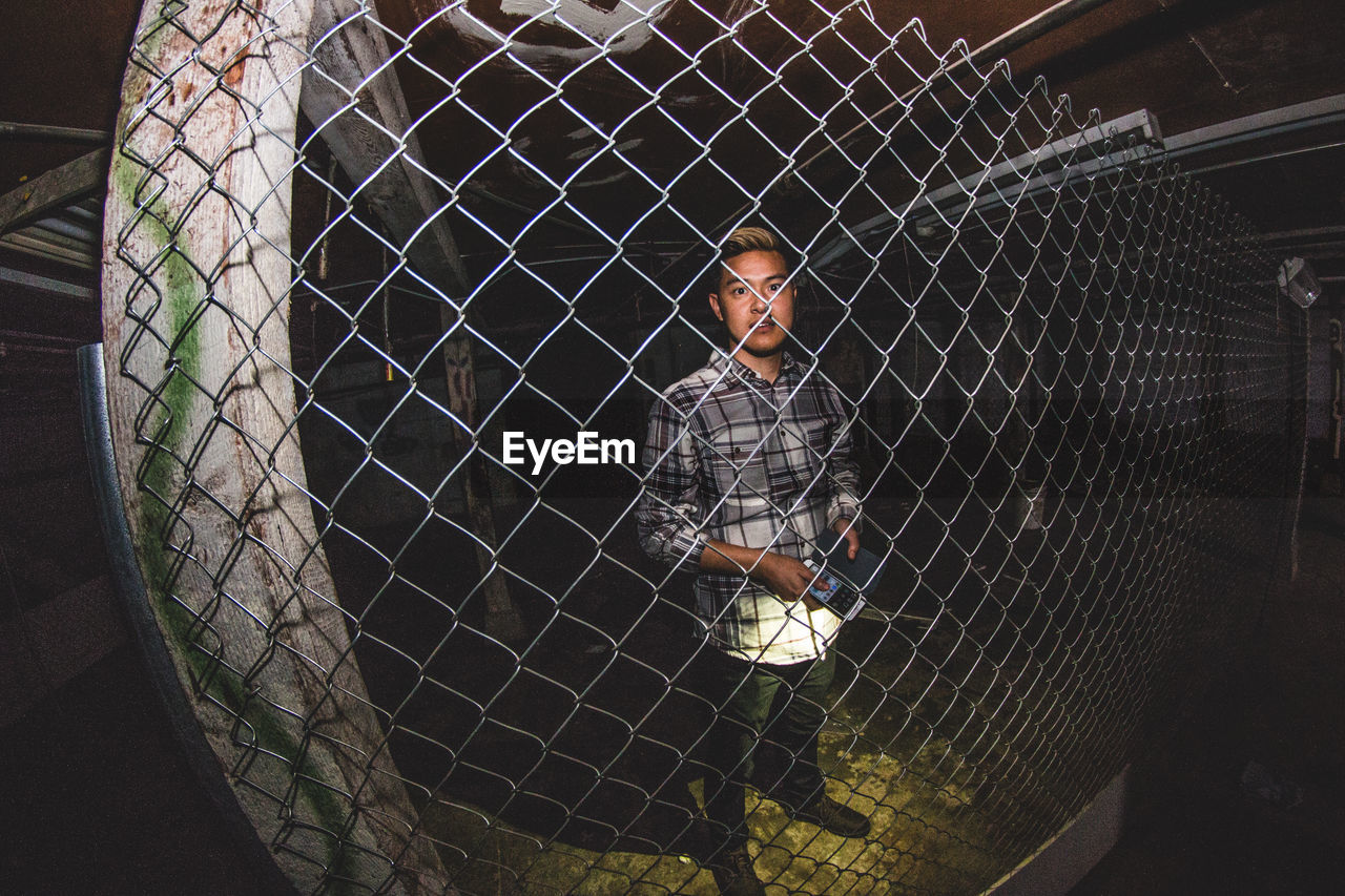 MAN SEEN THROUGH CHAINLINK FENCE IN CAGE AT NIGHT