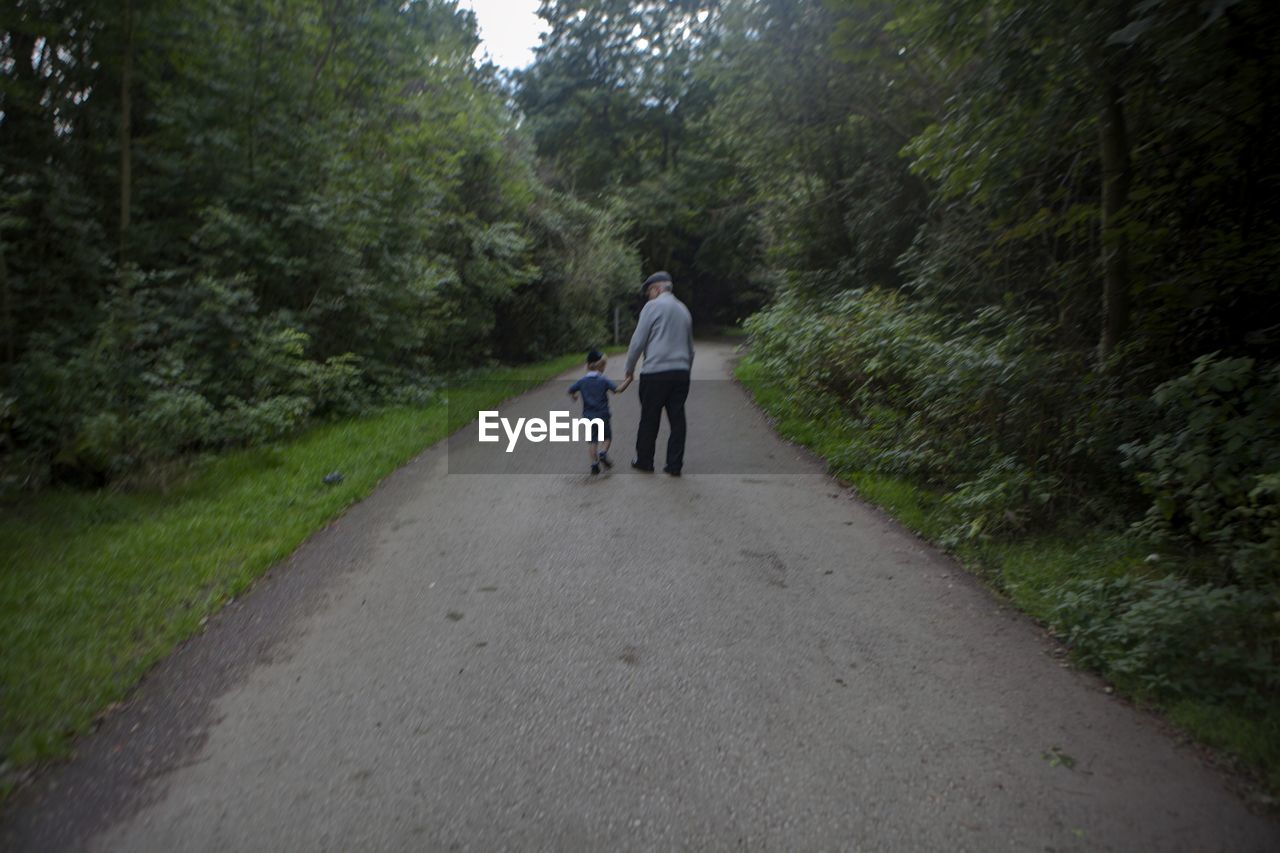 REAR VIEW OF PEOPLE WALKING ON ROAD AMIDST TREES