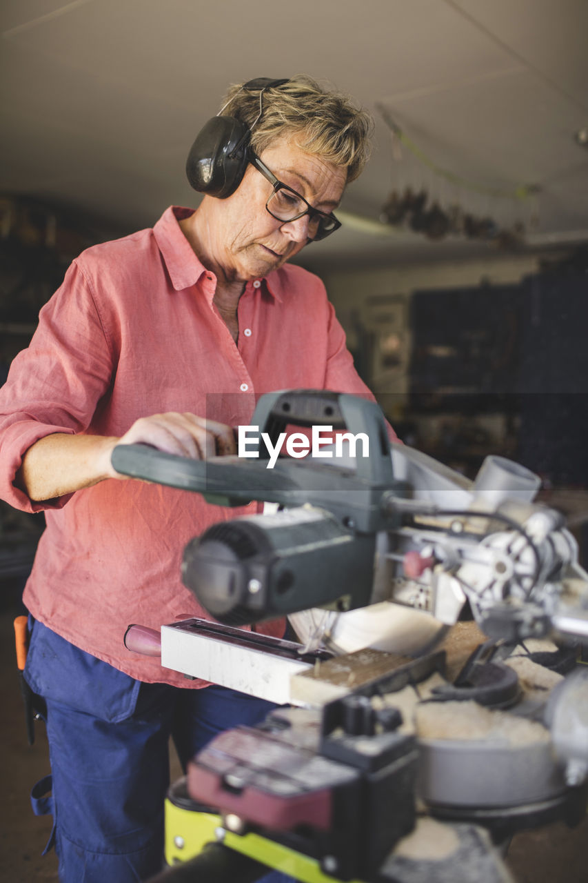 Senior woman using circular saw at workshop