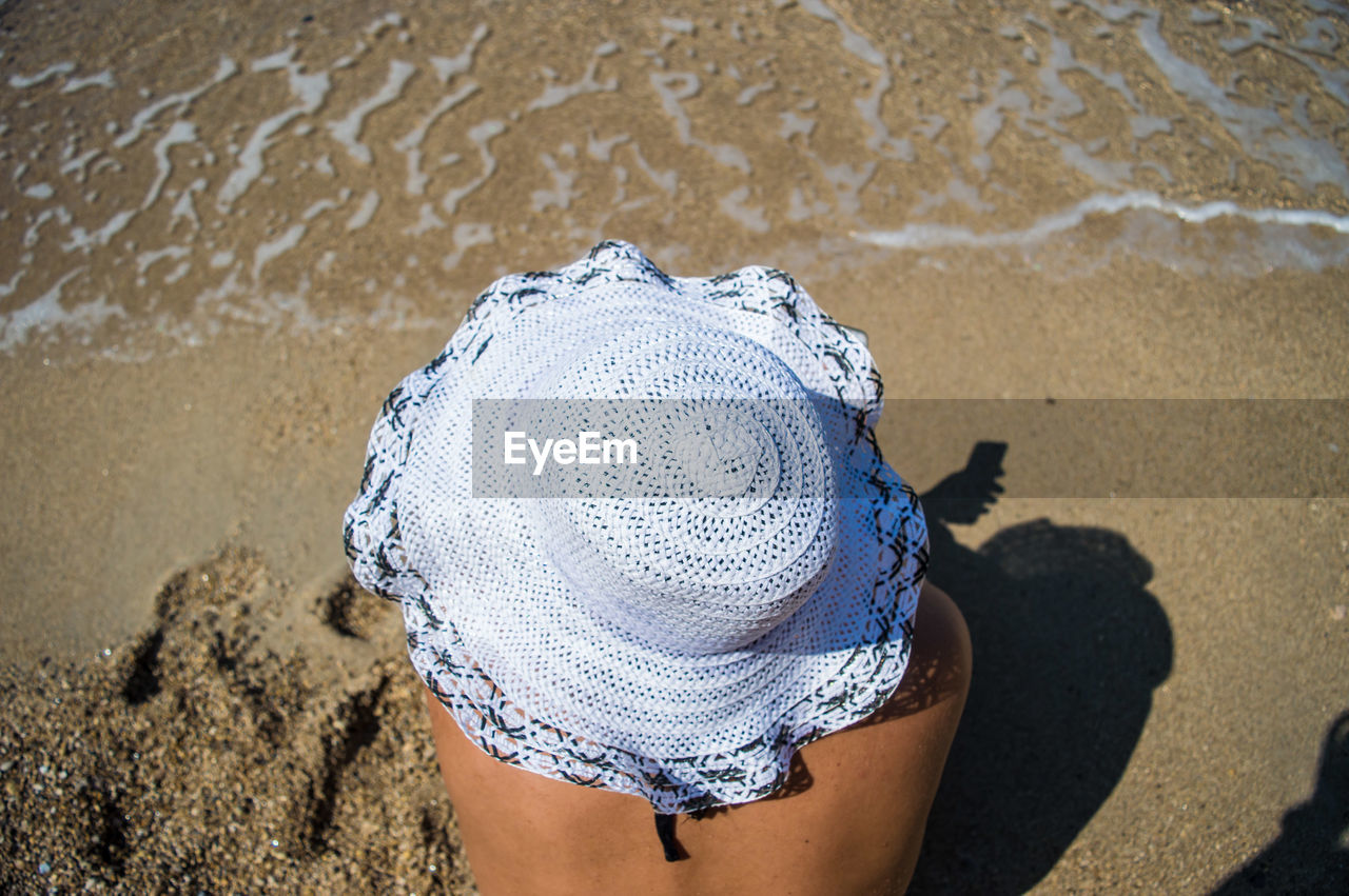 High angle view of woman wearing sun hat while sitting at beach on sunny day
