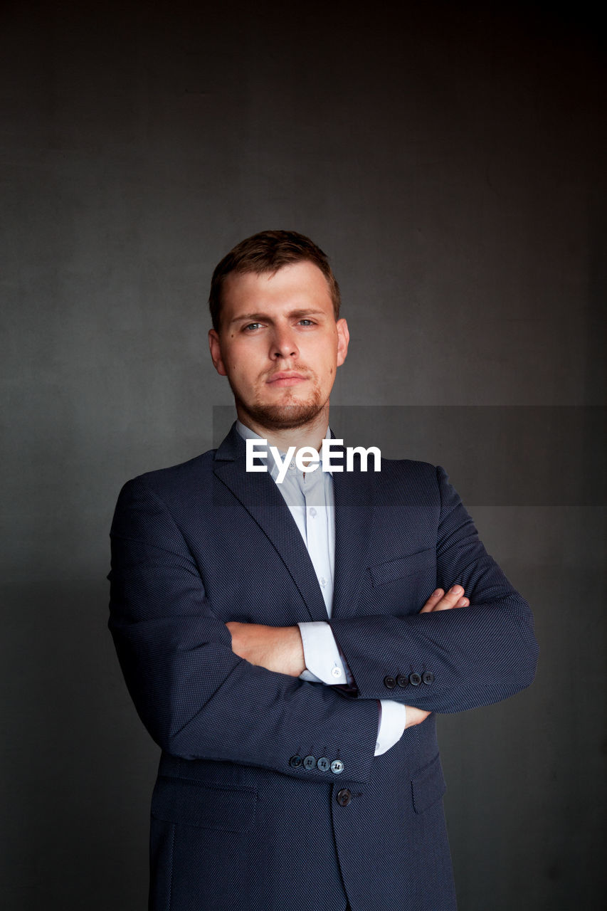 Portrait of well-dressed confident businessman with arms crossed standing against wall