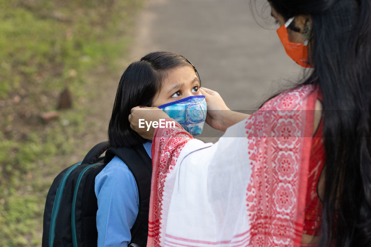 An indian school girl child going to school again after pandemic with her mother wearing nose mask 