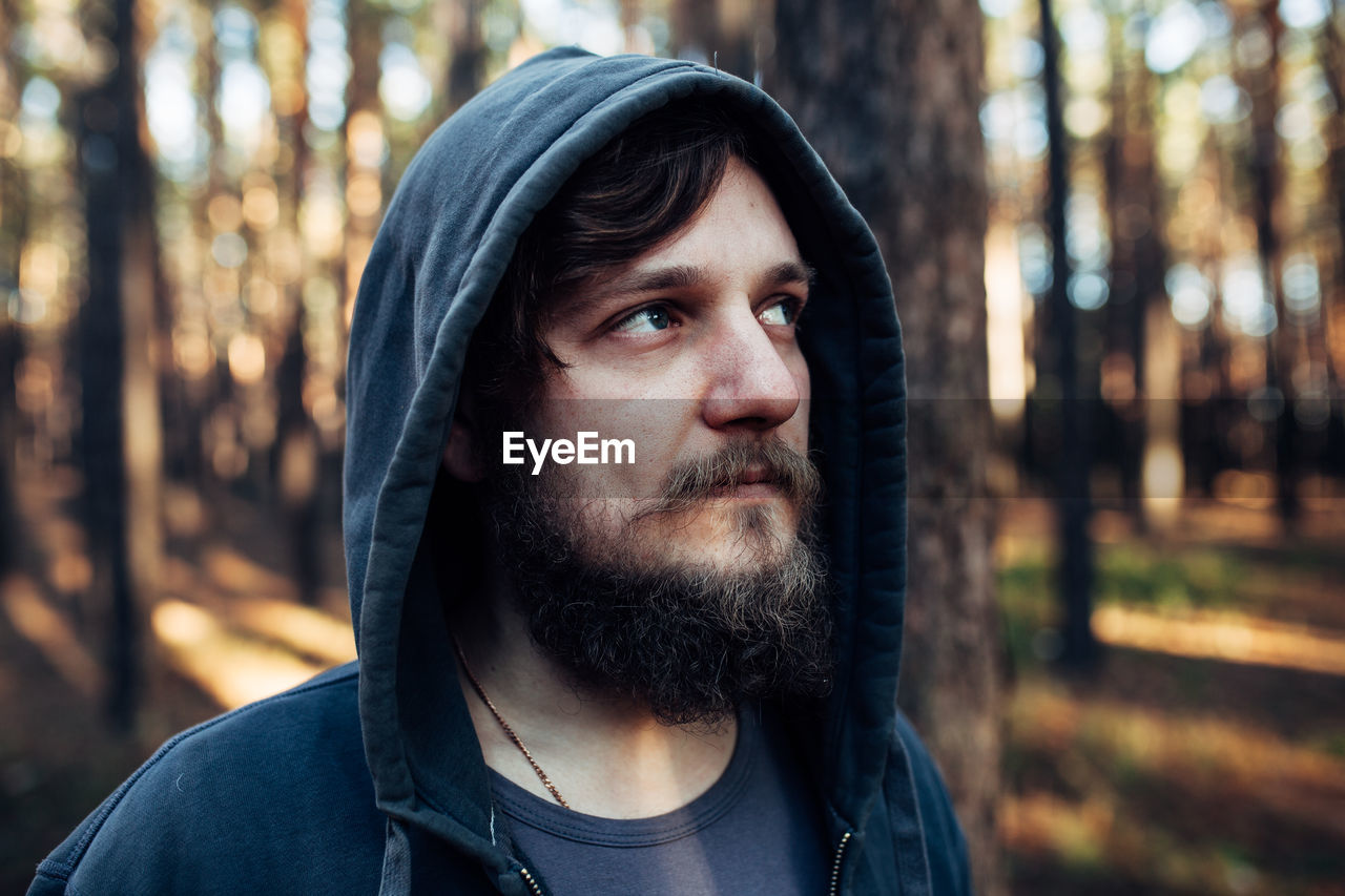 Close-up of mid adult man wearing hood looking away in forest