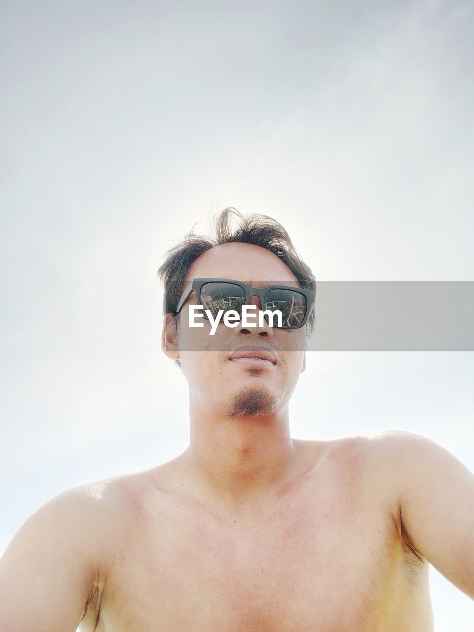 portrait of shirtless young man wearing sunglasses against sky