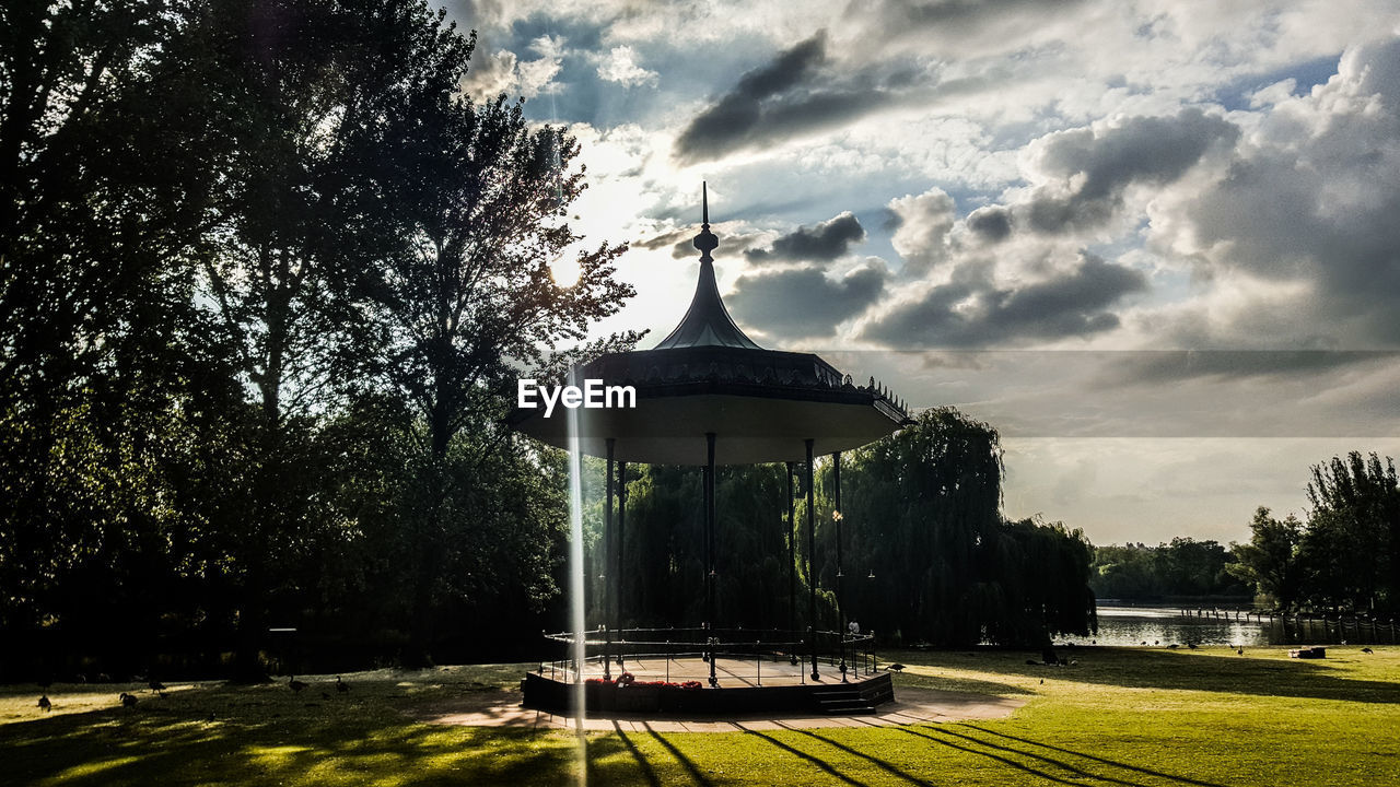 Gazebo on field by trees against sky