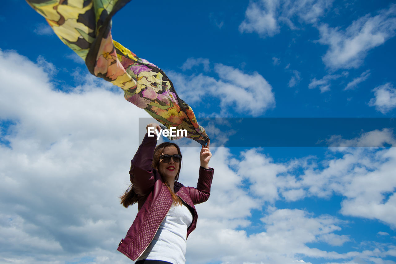 Low angle view of woman holding fabric against sky