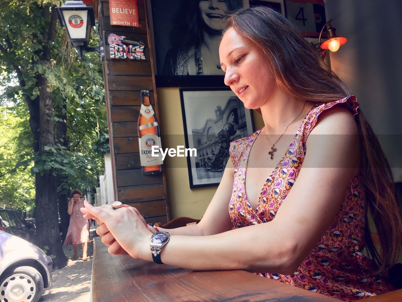 YOUNG WOMAN SITTING ON TABLE AT OUTDOOR CAFE