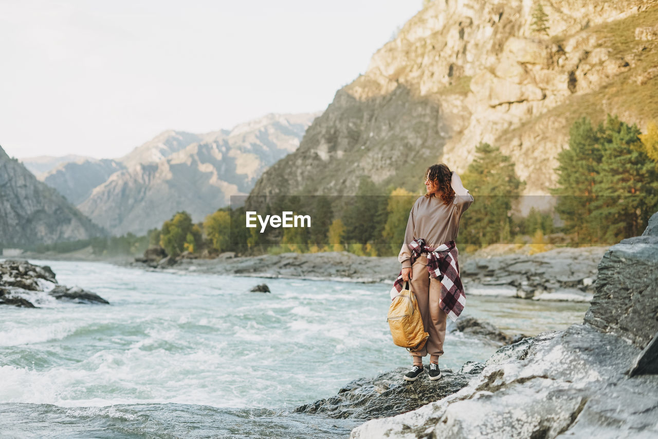 Young woman traveller in casual with backpack on mountain river on the sunset