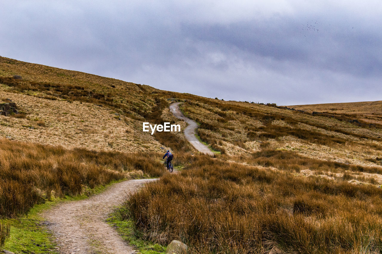 Man on road amidst field against sky