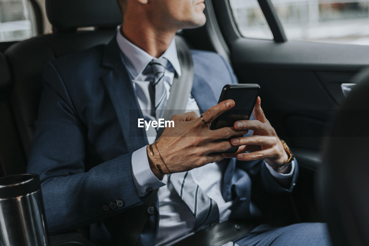 Midsection of businessman holding smart phone while sitting in car