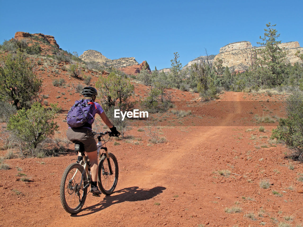 Woman riding bicycle on dirt road against sky