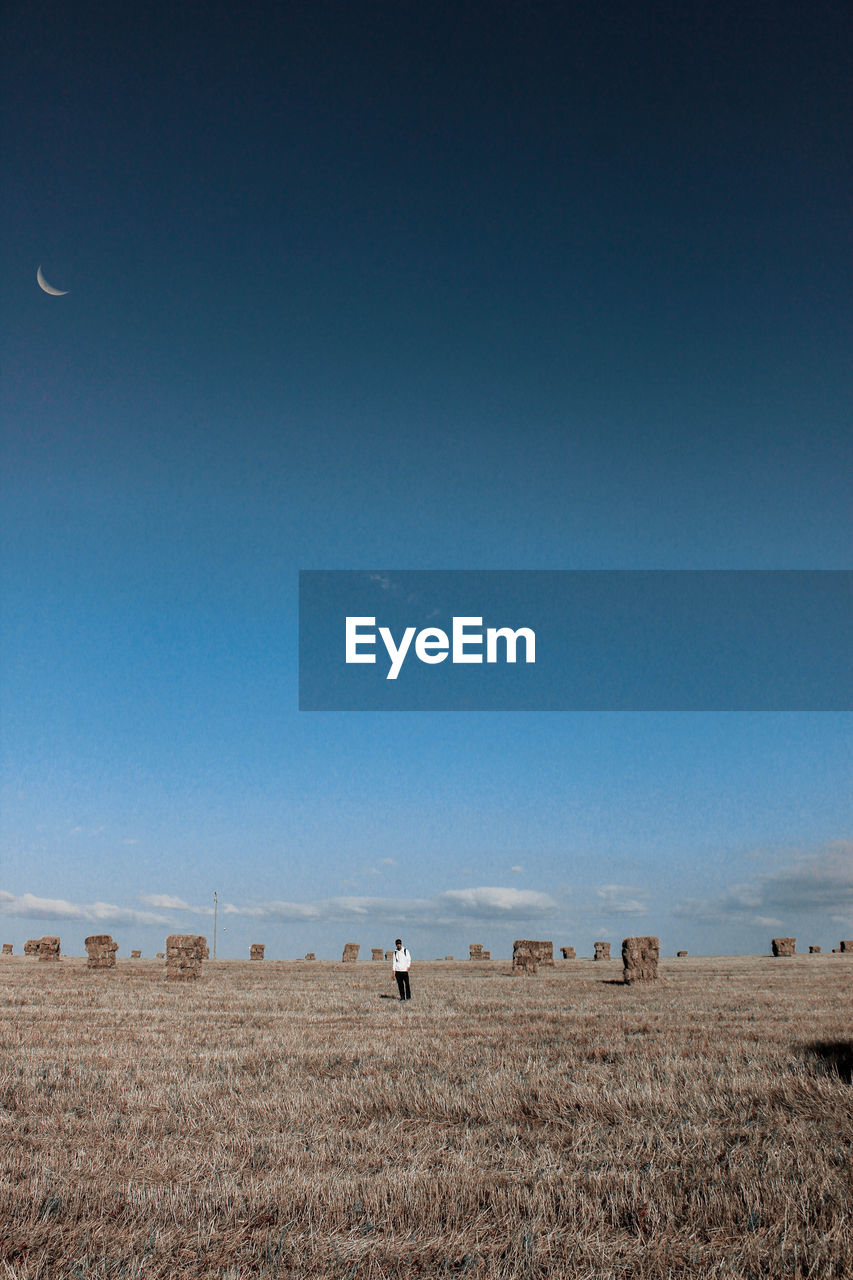 Mid distance view of man standing on grassy field against blue sky