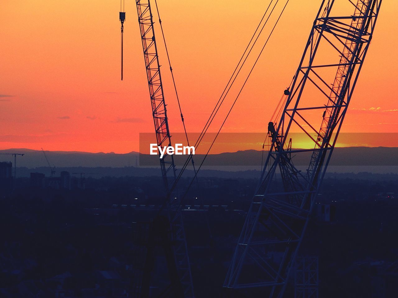 Cranes at construction site against orange sky