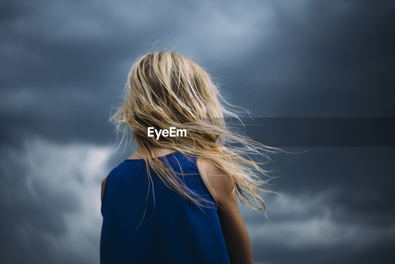 Low angle view of girl standing against cloudy sky