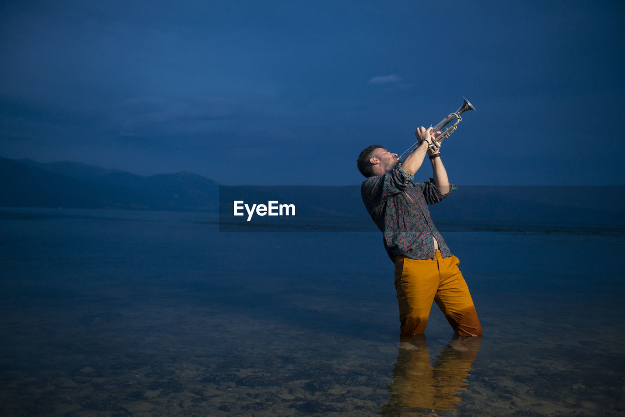 Man playing trumpet while standing in sea at night