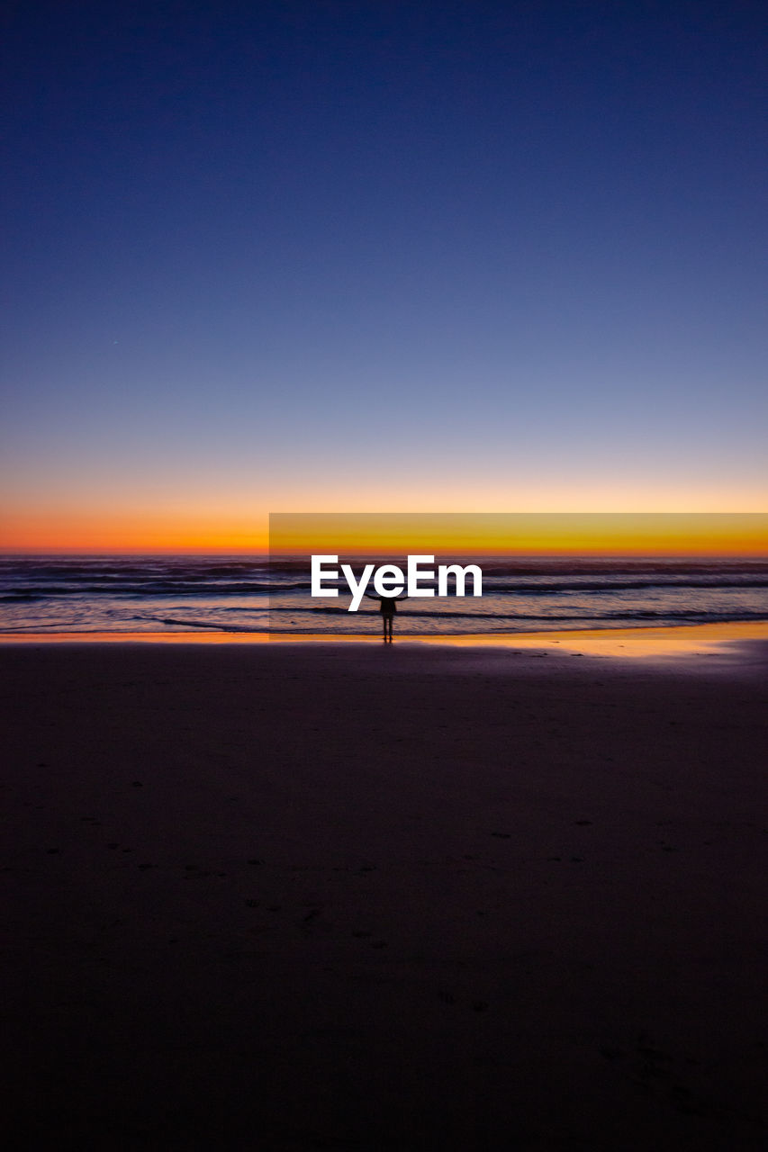 Scenic view of beach against sky during sunset with a person standing in the middle