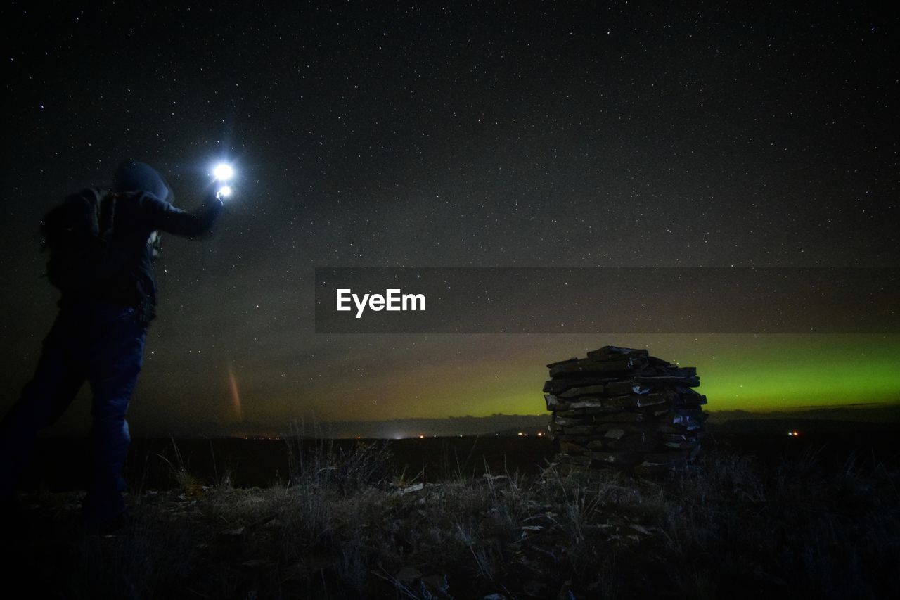 Low angle view of man with illuminated light standing on land against star field