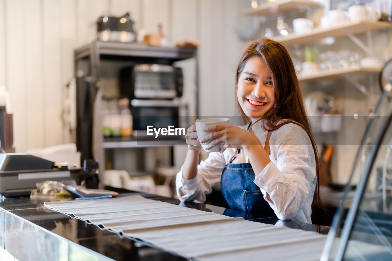 PORTRAIT OF SMILING WOMAN SITTING ON TABLE