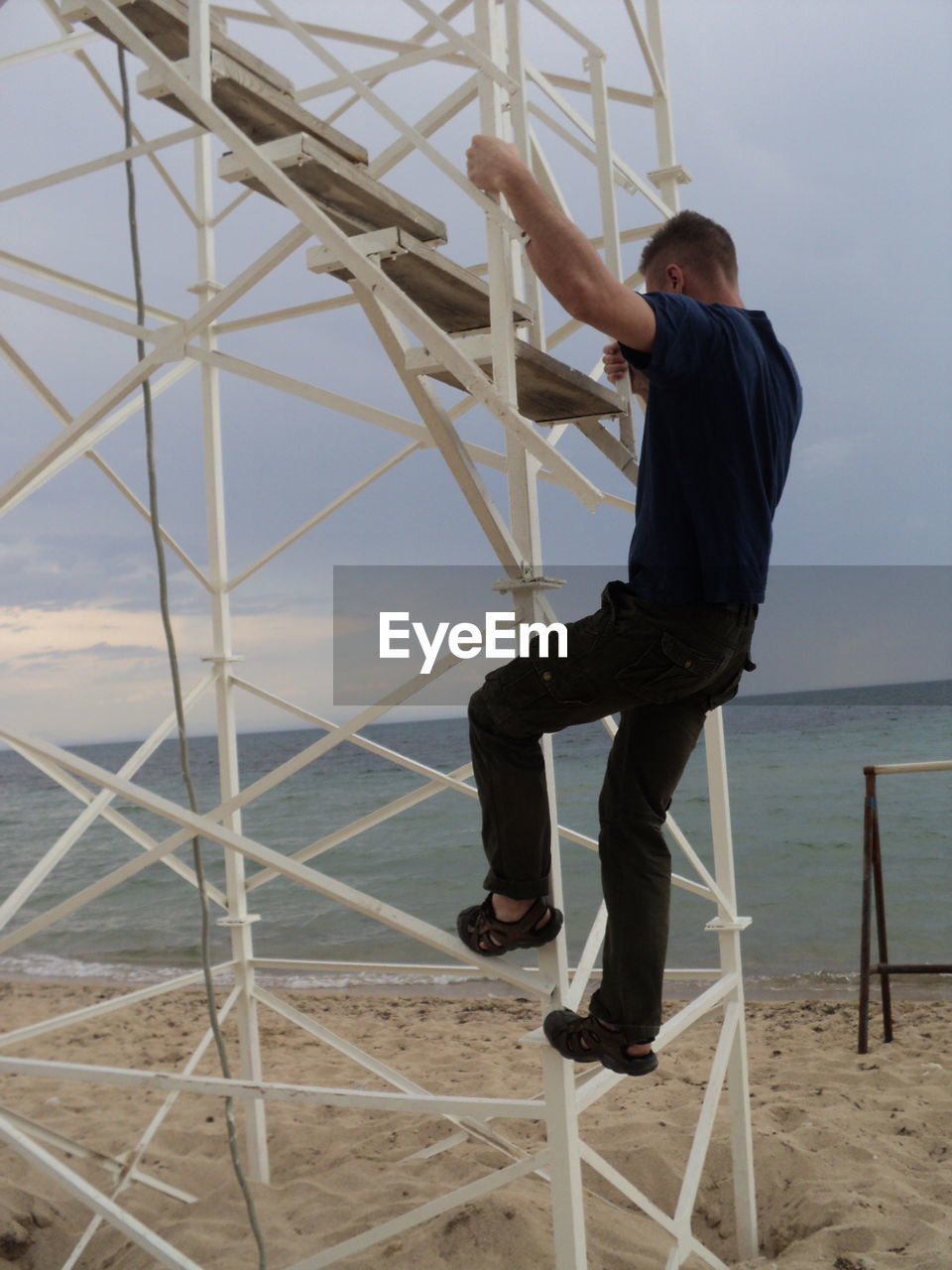 Mid adult man climbing on metallic structure of lookout tower at beach