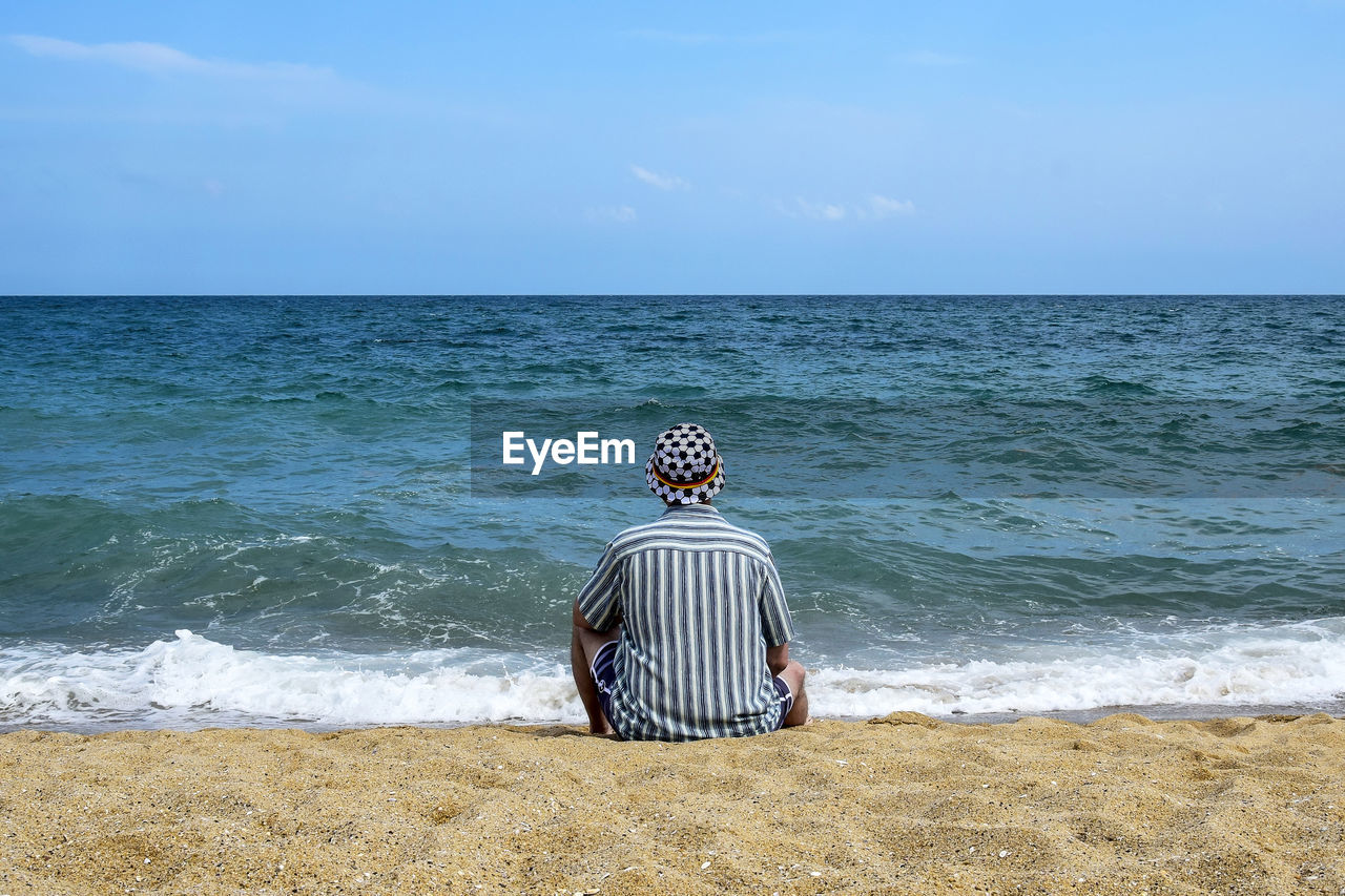 Man sits on the seashore and relaxes. looks into the boundless blue distance. copy space.