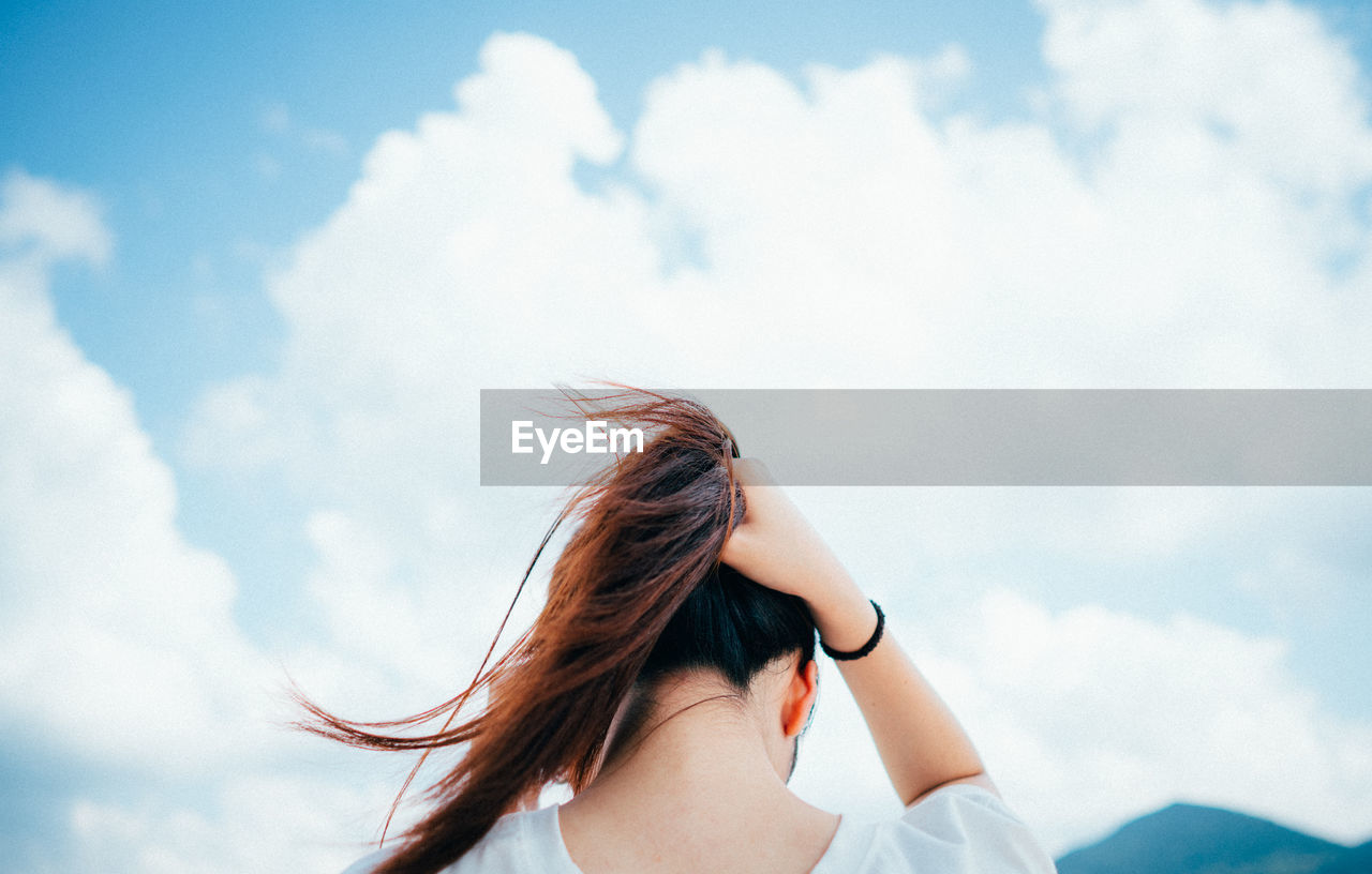 Young woman looking away against sky