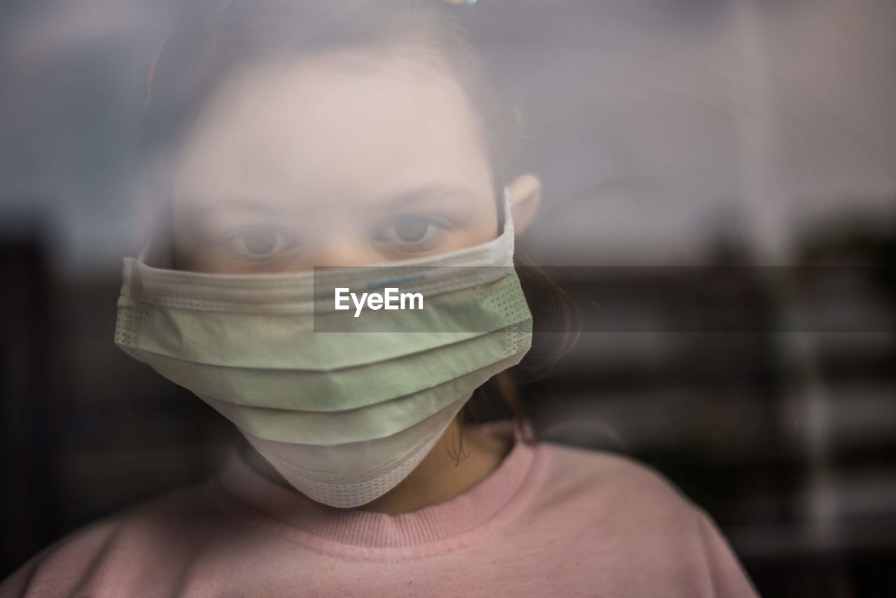 Close-up portrait of girl wearing mask looking through window