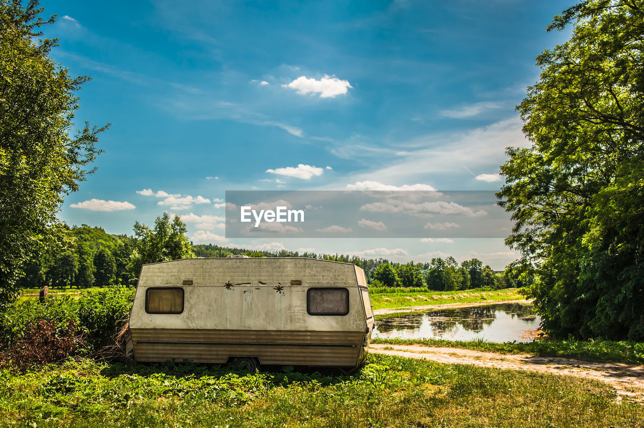 Vehicle on field by lake against cloudy sky during sunny day