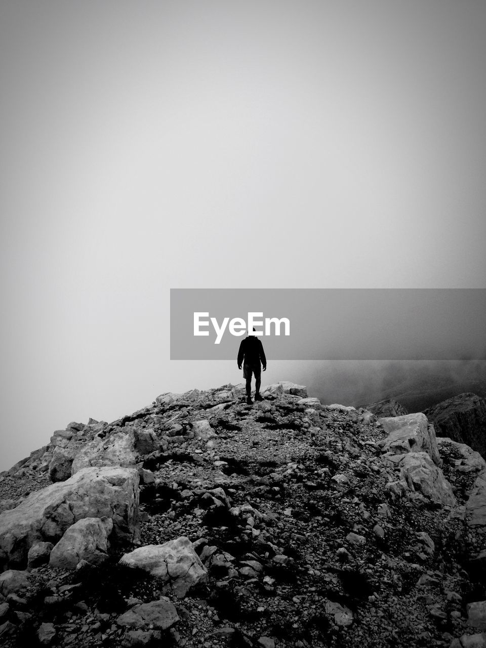 Silhouette hiker standing on mountain against sky during foggy weather