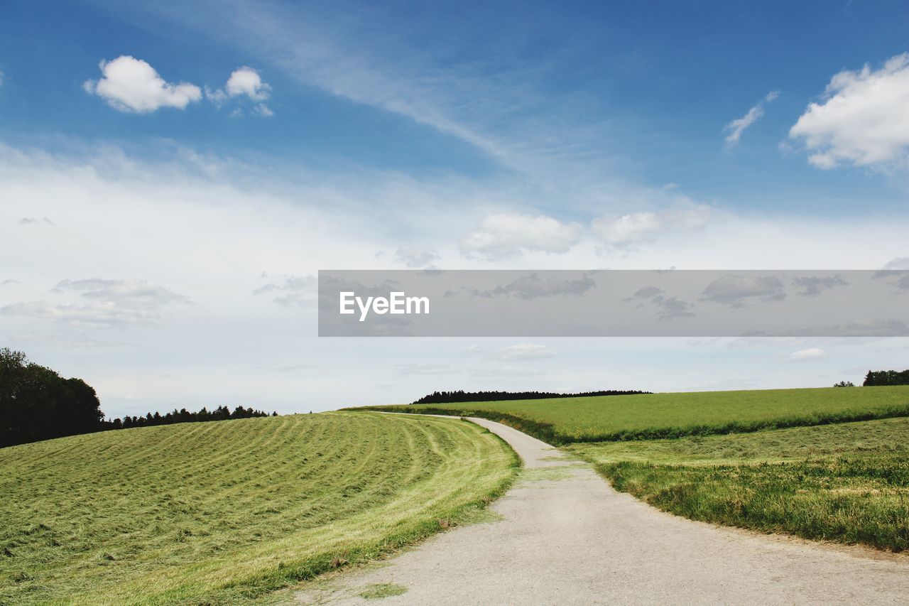 Empty road amidst field against sky