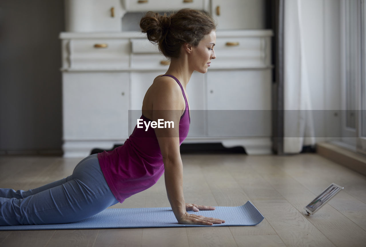 Mid adult woman watching digital tablet while doing yoga at home