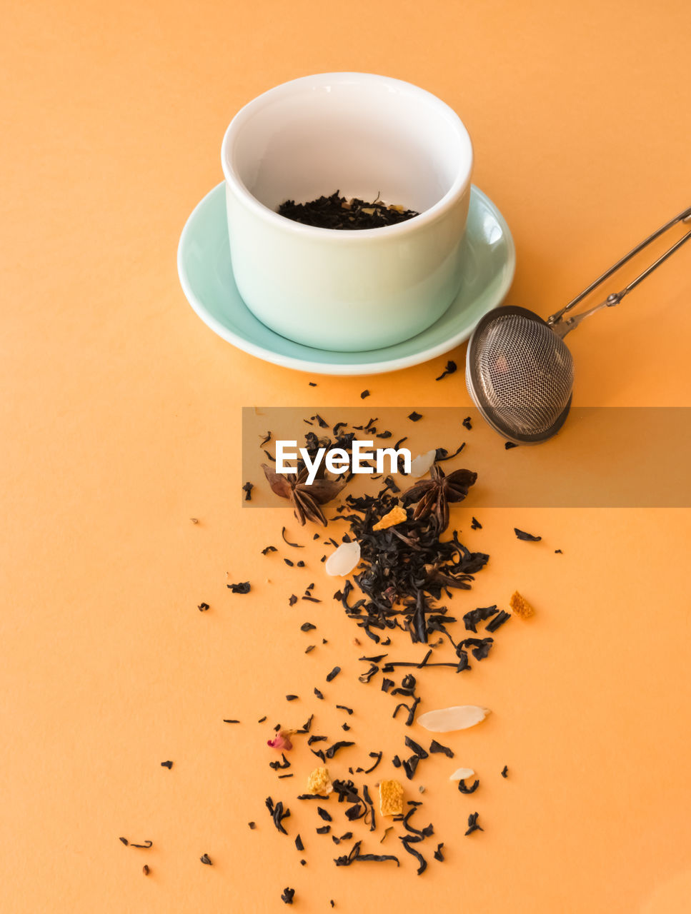 'tea preparing ceremony,  cup, tea strainer and black fruit herbal dry tea on orange background. '