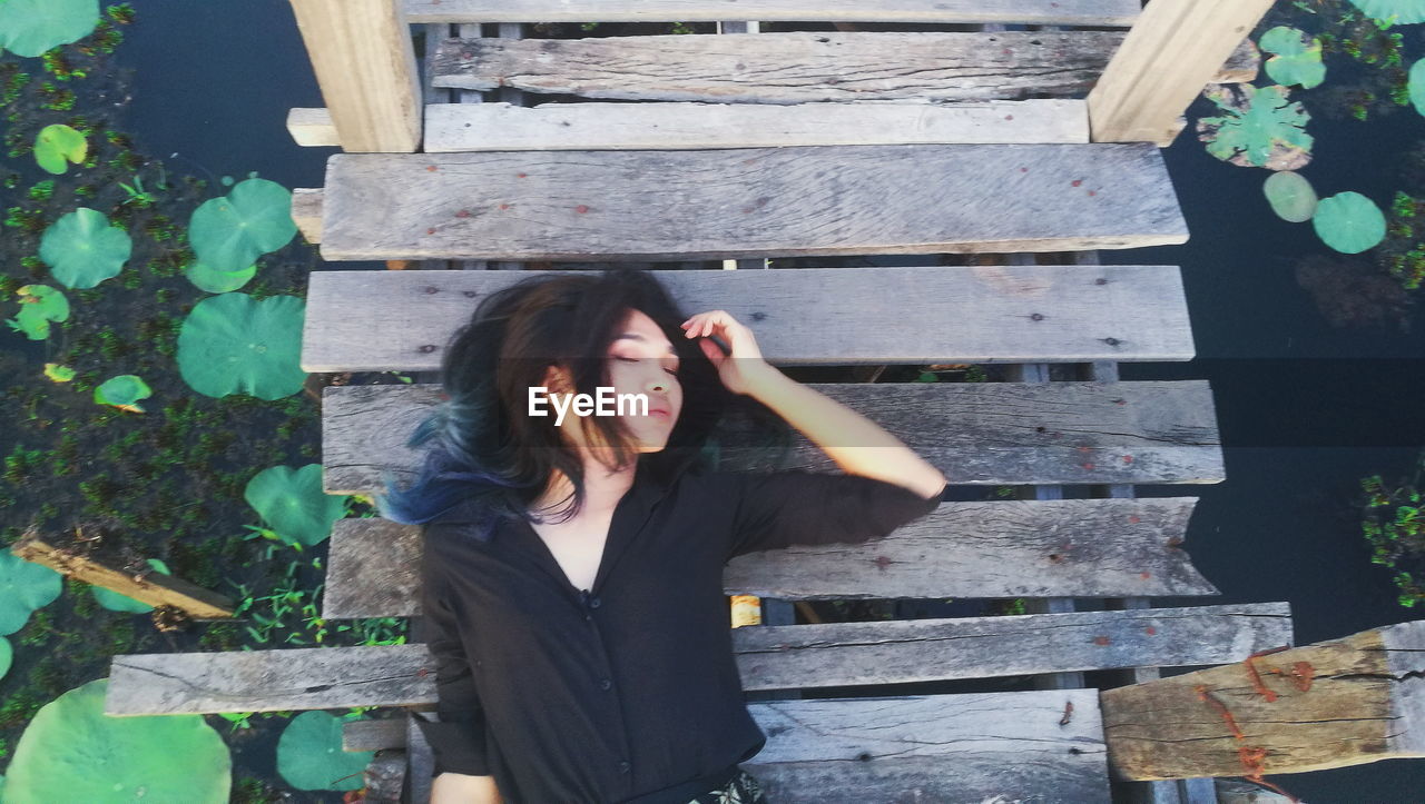 High angle view of young woman lying on pier over pond