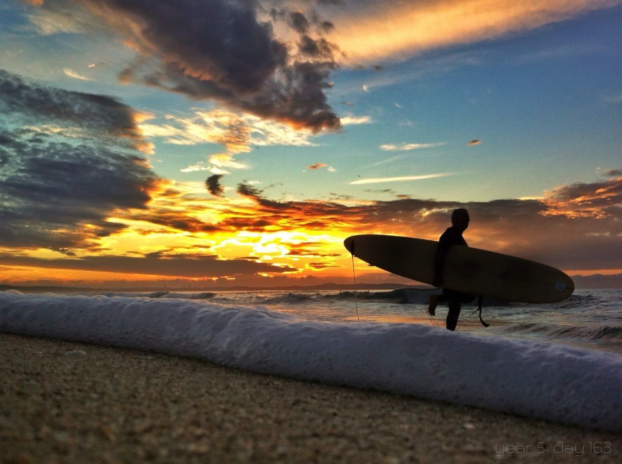 Silhouette man carrying surfboard on beach at sunset