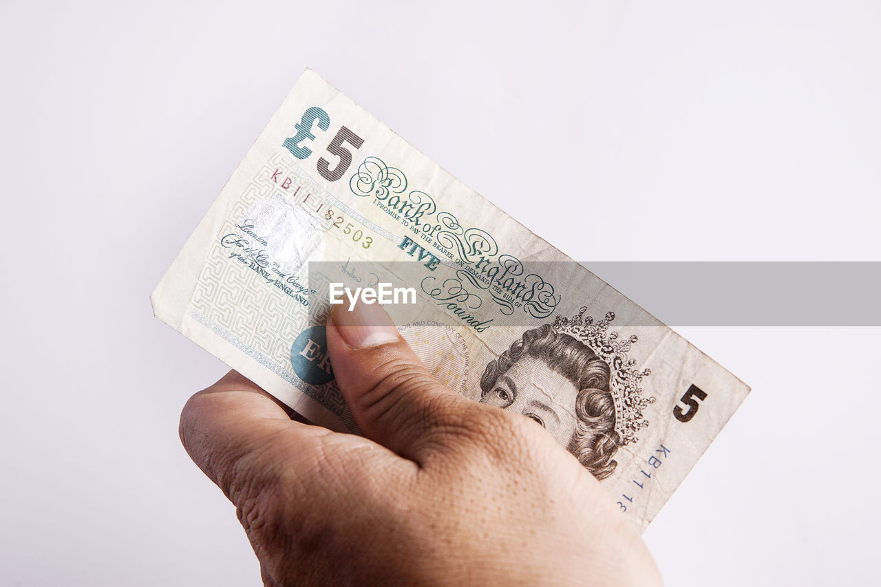 Cropped hand of person holding british currency against white background