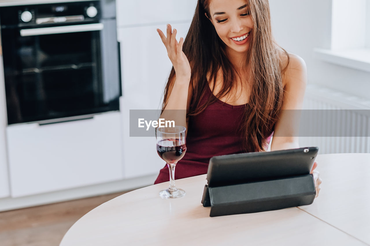 YOUNG WOMAN USING MOBILE PHONE WHILE SITTING ON TABLE