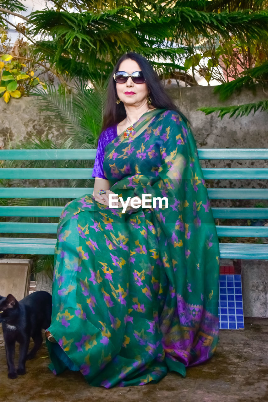 one person, fashion, women, animal themes, adult, animal, young adult, portrait, one animal, mammal, clothing, domestic animals, pet, full length, looking at camera, sitting, glasses, dress, front view, lifestyles, dog, sunglasses, green, plant, nature, female, standing, canine, leisure activity, hairstyle, outdoors, day, costume, tree, spring, traditional clothing