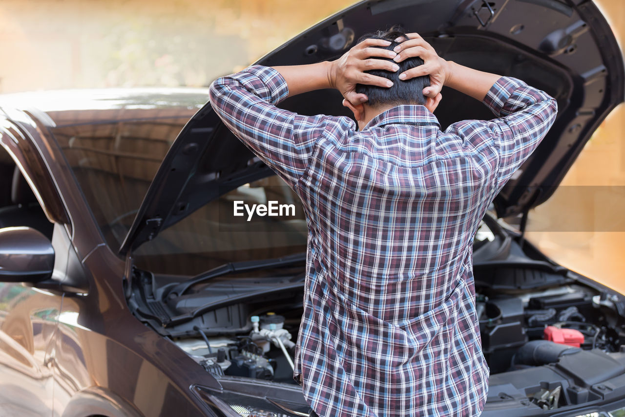 Rear view of man with hand in hair standing by car