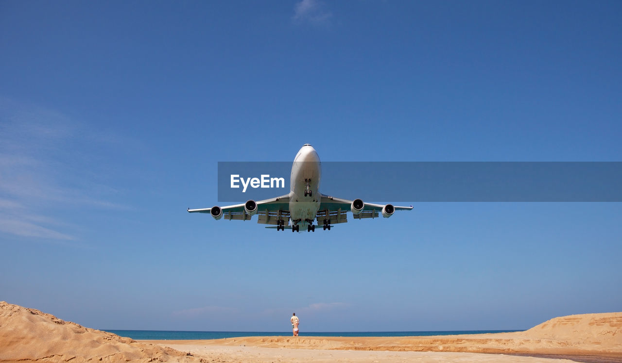 AIRPLANE FLYING OVER BEACH AGAINST SKY