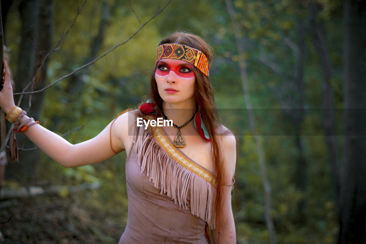 Young woman in traditional clothing looking away while standing in forest