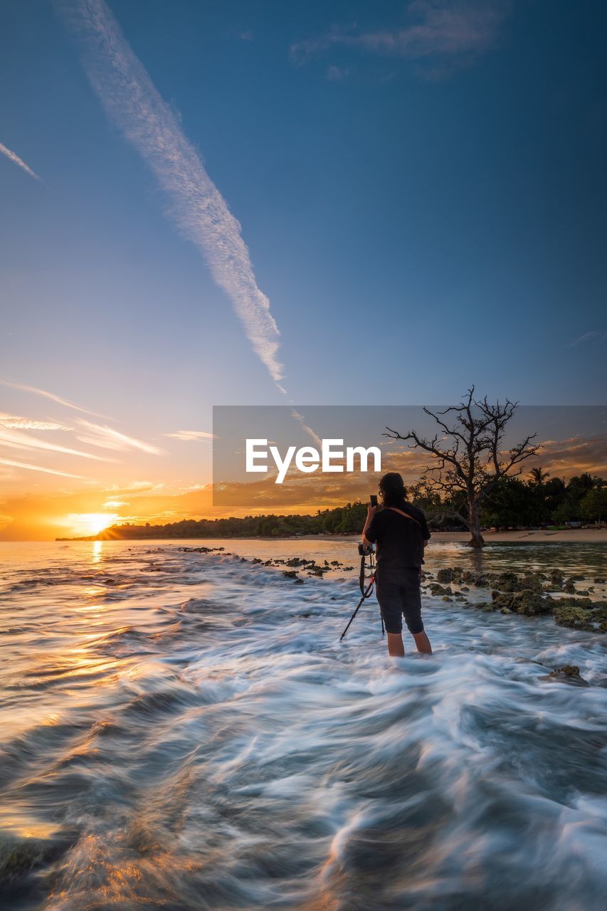 Rear view of man photographing at beach during sunset